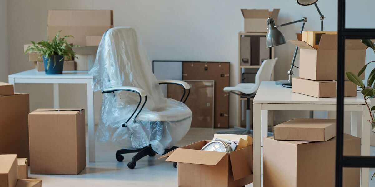 Packed office space with boxes, chairs covered in protective wrap, and desks, illustrating a detailed office move checklist.